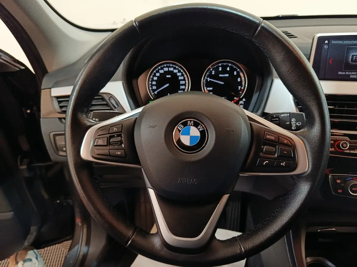 Vue rapprochée du volant cuir noir multifonctions d’un BMW X1 2021, avec tableau de bord et écran digital visibles.