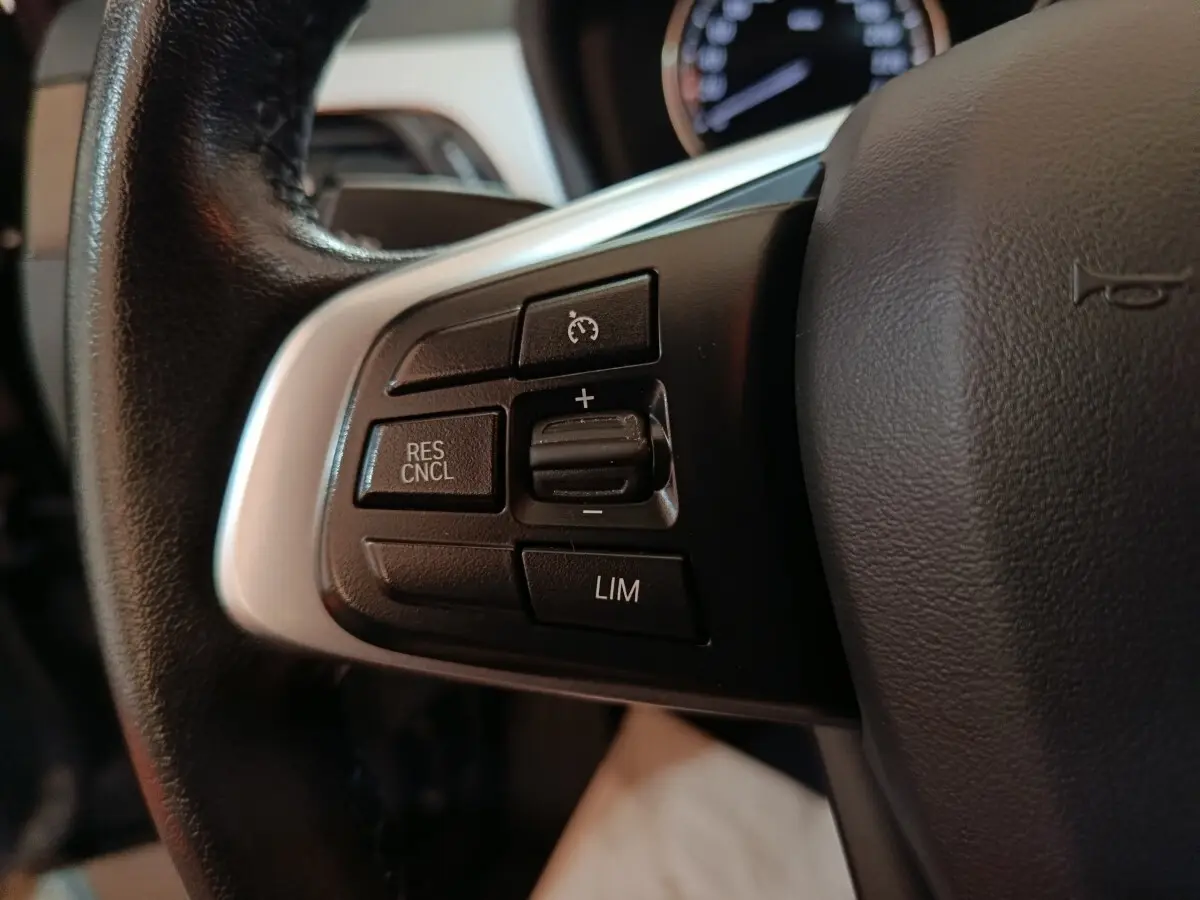 Gros plan sur les commandes du régulateur de vitesse au volant cuir noir d’un BMW X1 gris foncé 2021.