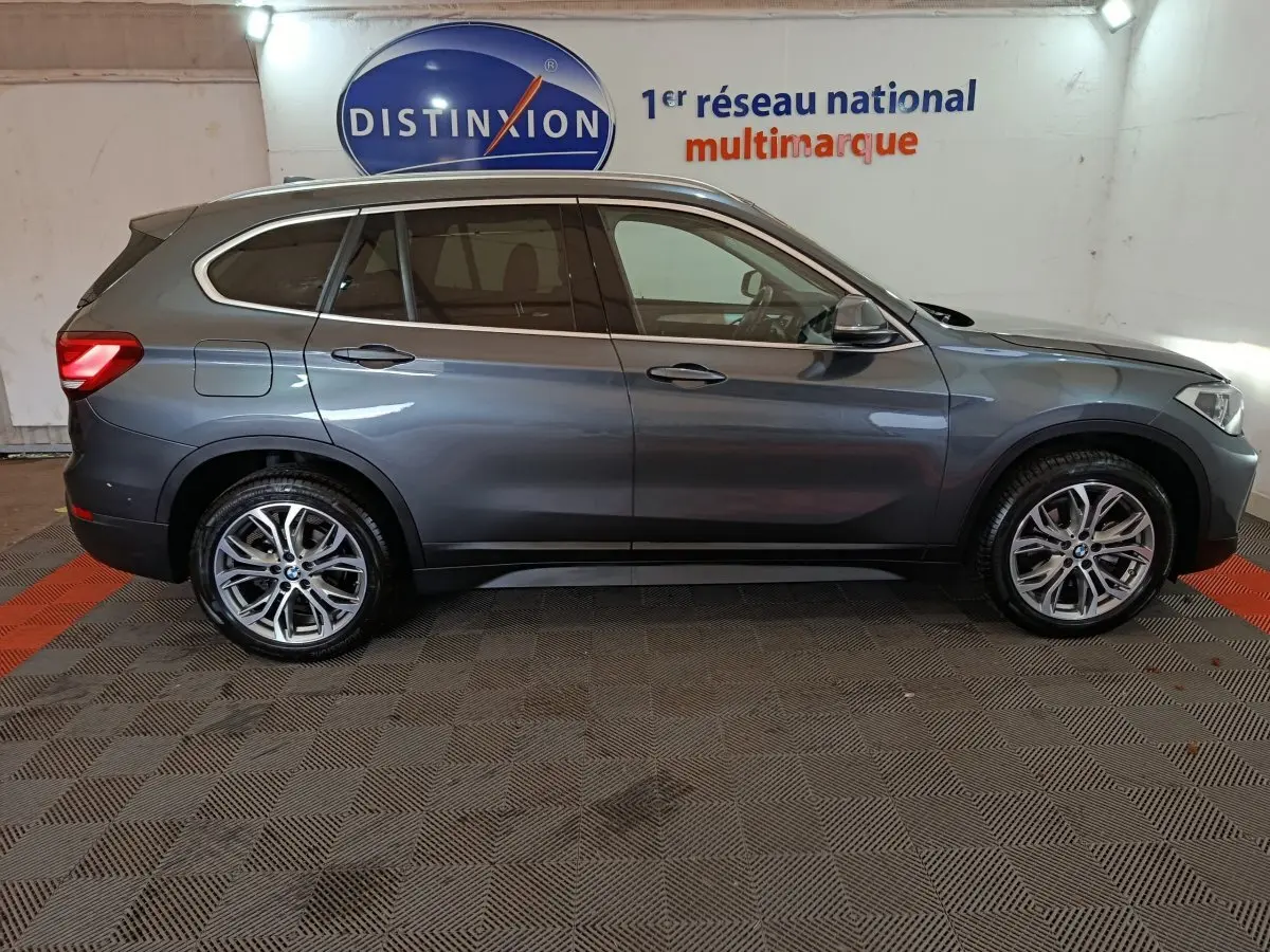 BMW X1 sDrive18i Lounge gris foncé vue de profil côté gauche, avec jantes alliage et vitres teintées, en intérieur showroom.