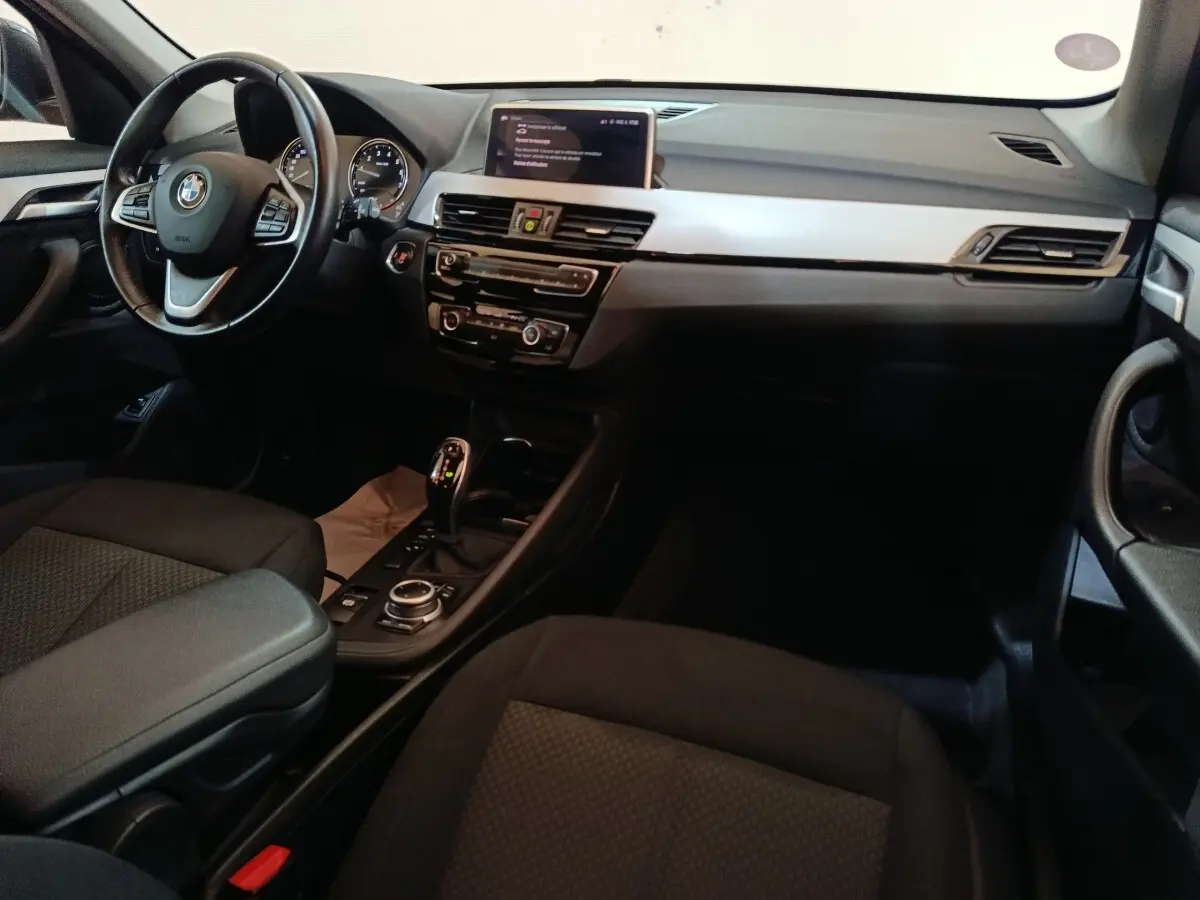 Intérieur BMW X1 sDrive18i 2021 vu côté conducteur, tableau de bord noir avec écran central et volant cuir multifonctions.