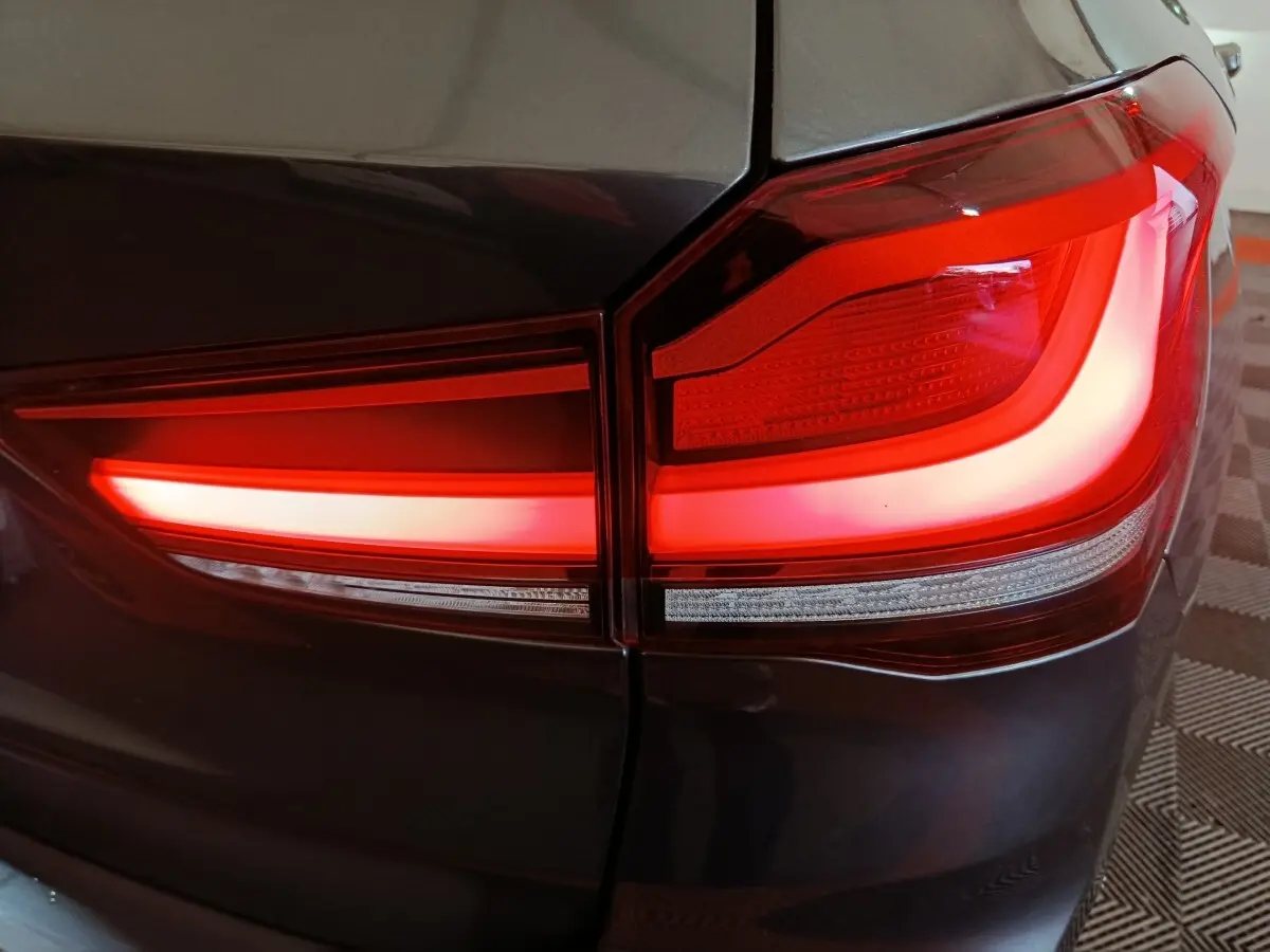 Gros plan sur le feu arrière droit rouge vif d’un BMW X1 sDrive18i Lounge gris foncé, avec carrosserie brillante.