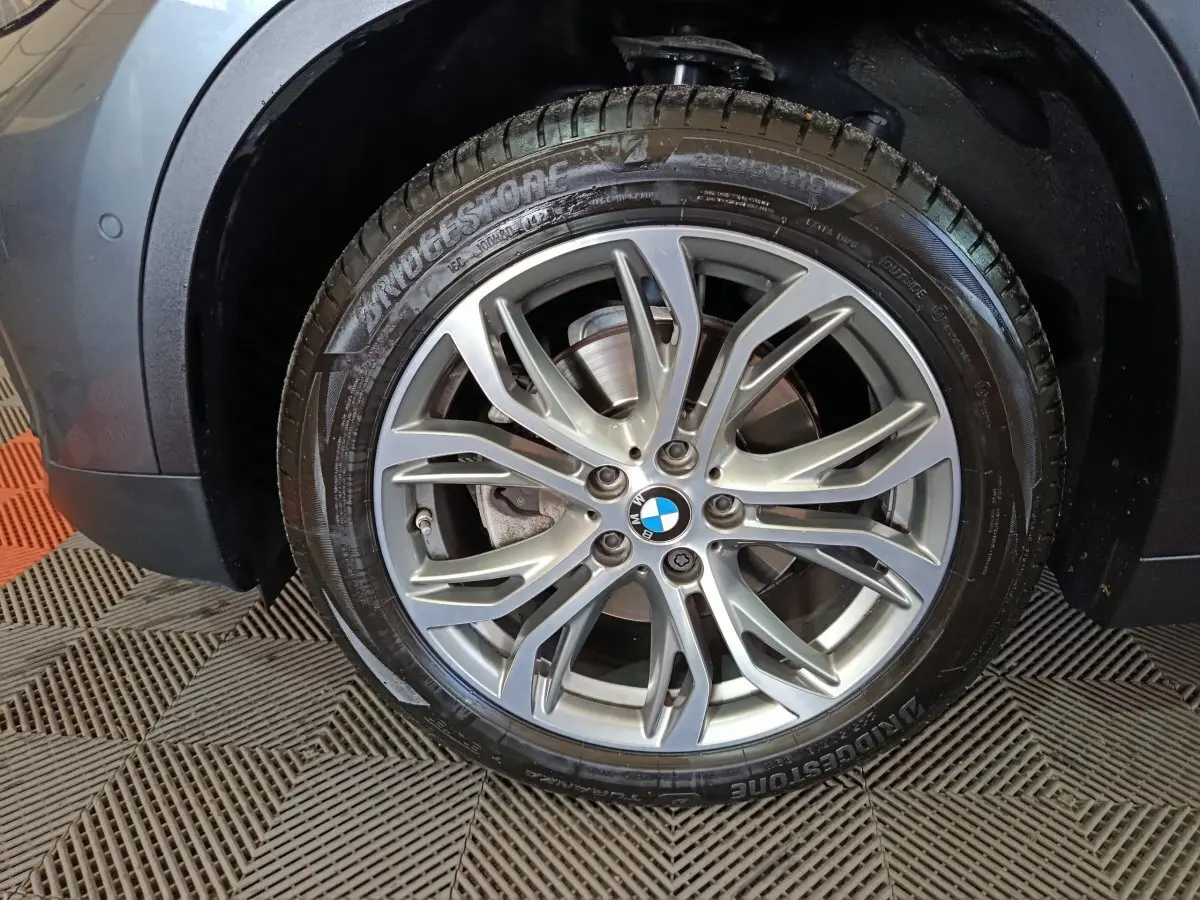 Gros plan sur la roue avant gauche d’un BMW X1 gris foncé avec jante alliage et pneu Bridgestone.