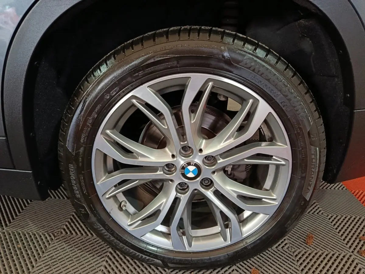 Gros plan sur la roue avant droite d'une BMW X1 gris foncé, mettant en valeur la jante alliage à dix branches.