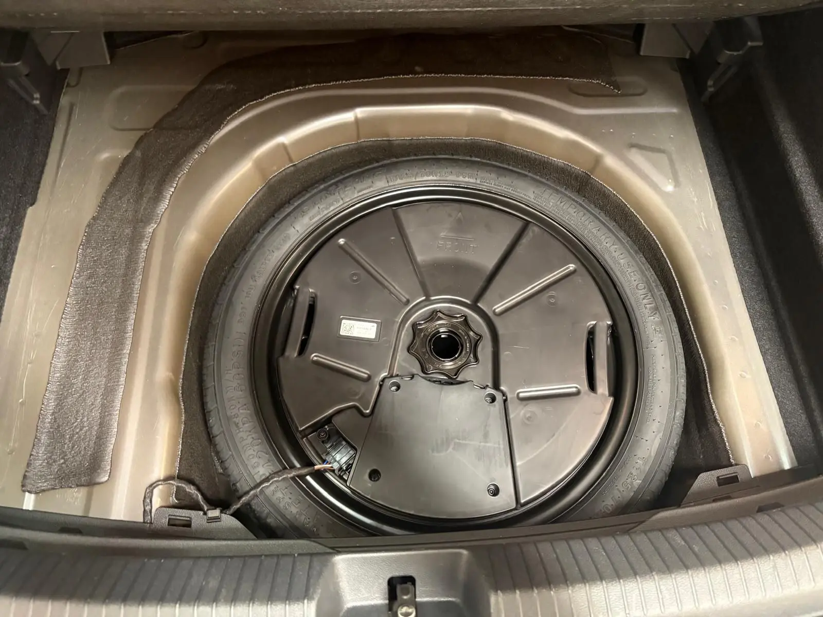 Gros plan sur la roue de secours compacte du Volkswagen Taigo 2024, logée dans le coffre, avec son cache noir circulaire.