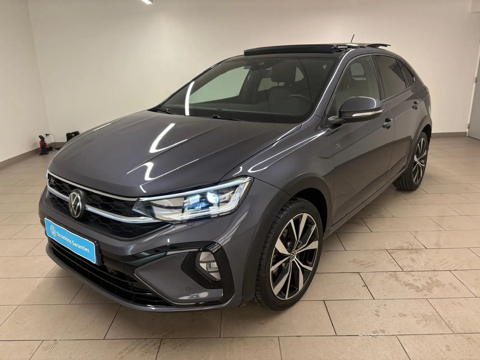 Volkswagen Taigo gris cendré en 3/4 avant droit, avec jantes noires brillantes et toit ouvrant électrique.