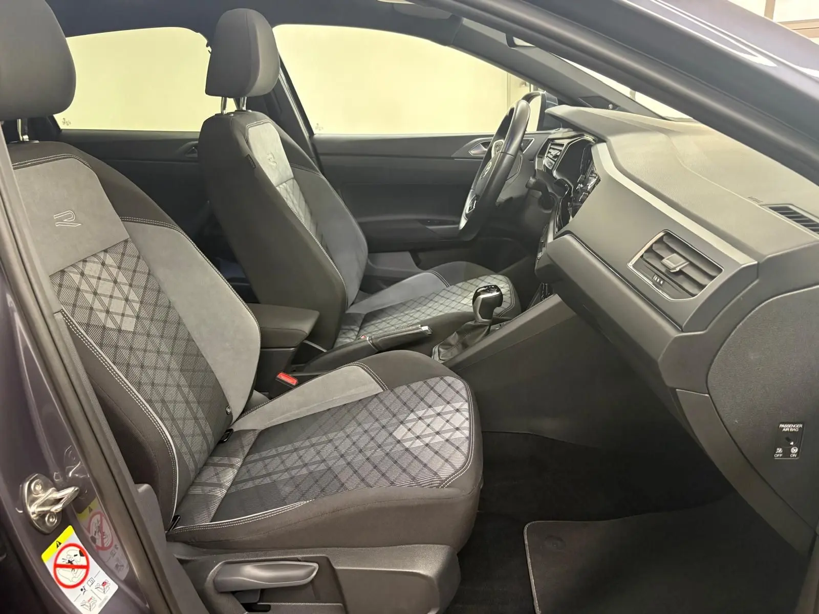 Vue intérieure côté gauche du Volkswagen Taigo 1.5 TSI R-Line 2024, sièges avant en tissu gris à motifs et volant visible.