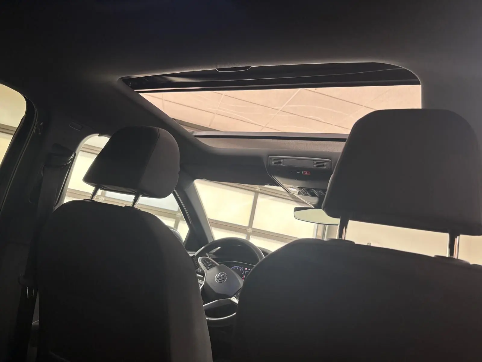 Vue intérieure depuis l'arrière montrant le toit ouvrant en verre et le volant du Volkswagen Taigo gris cendré 2024.