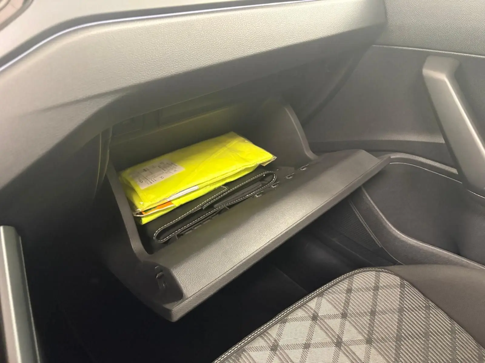 Vue intérieure du coffre à gants ouvert côté passager du Volkswagen Taigo gris cendré, avec documents jaunes visibles.