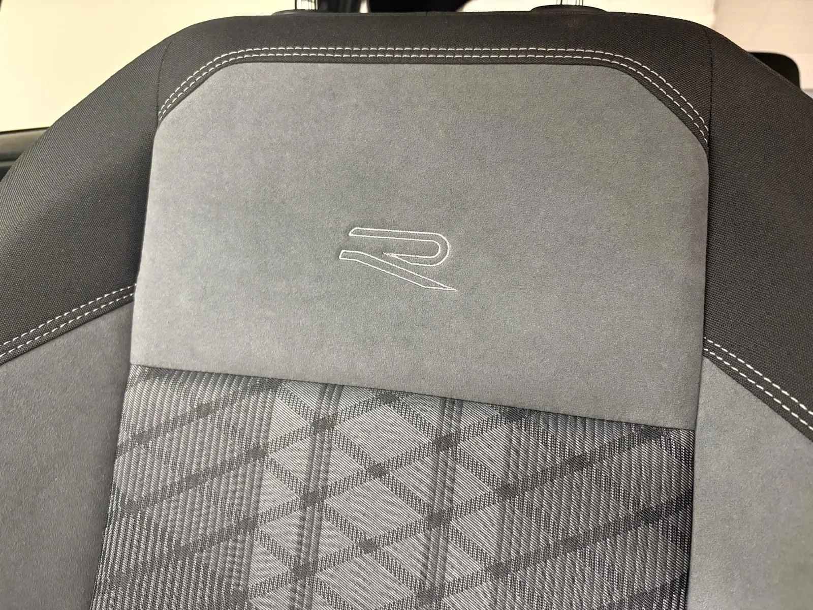 Détail du siège avant gris avec surpiqûres blanches et logo R brodé, intérieur Volkswagen Taigo 2024.