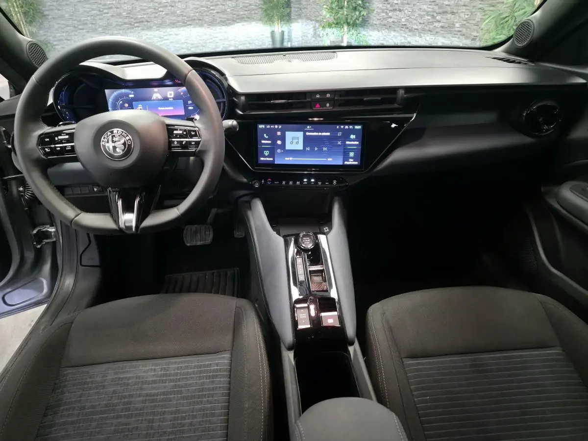Vue intérieure avant de l'Alfa Romeo Junior 1.2 Ibrida gris, avec tableau de bord digital et écran tactile central.