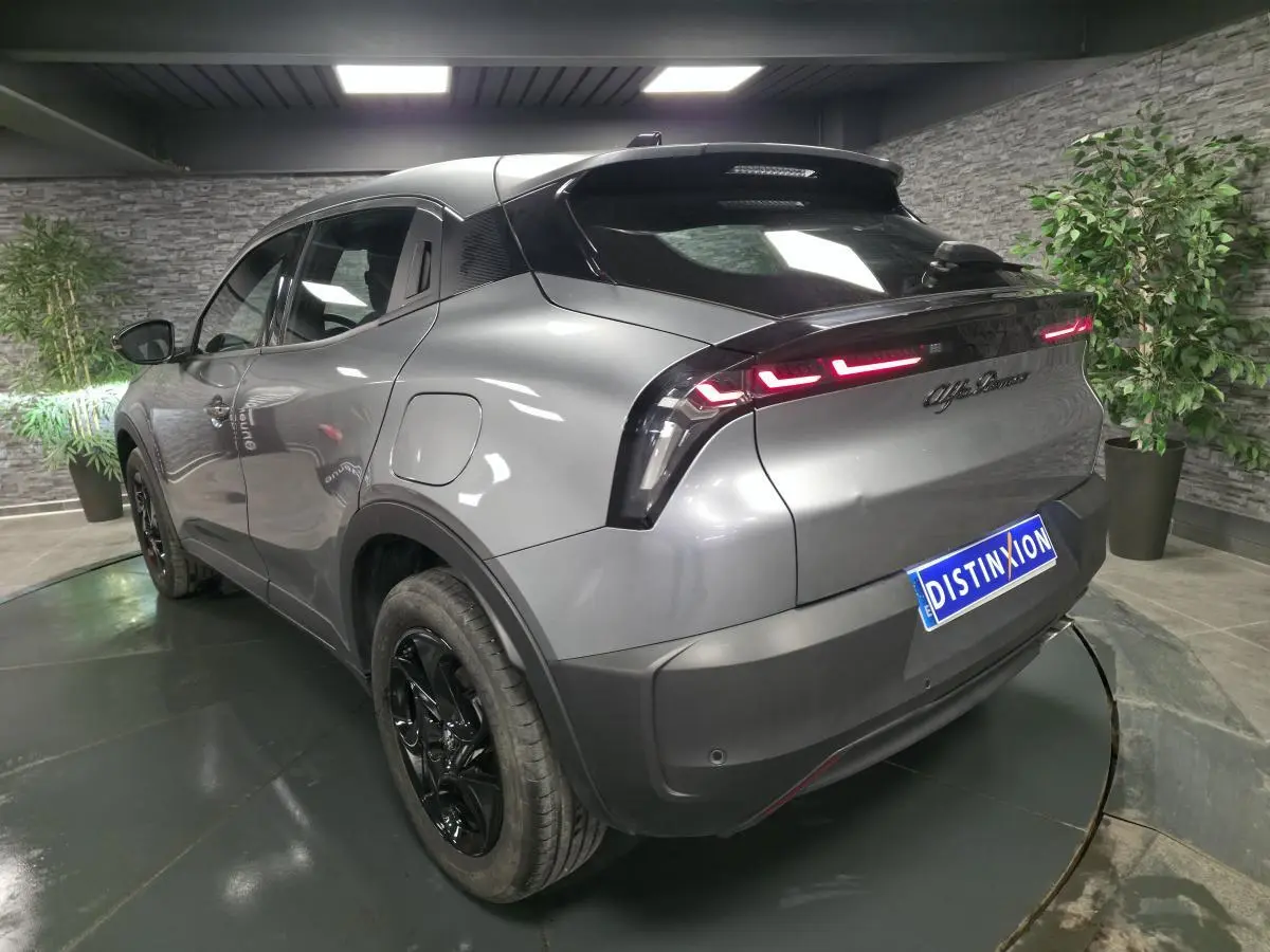 Vue 3/4 arrière gauche d'une Alfa Romeo Junior gris métallisé avec feux arrière LED et jantes noires brillantes.
