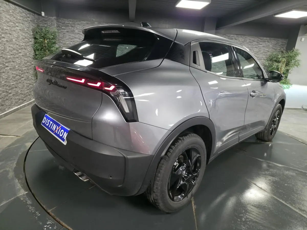 Vue 3/4 arrière droite de l'Alfa Romeo Junior 1.2 Ibrida gris métallisé avec jantes noires et feux arrière LED distinctifs.