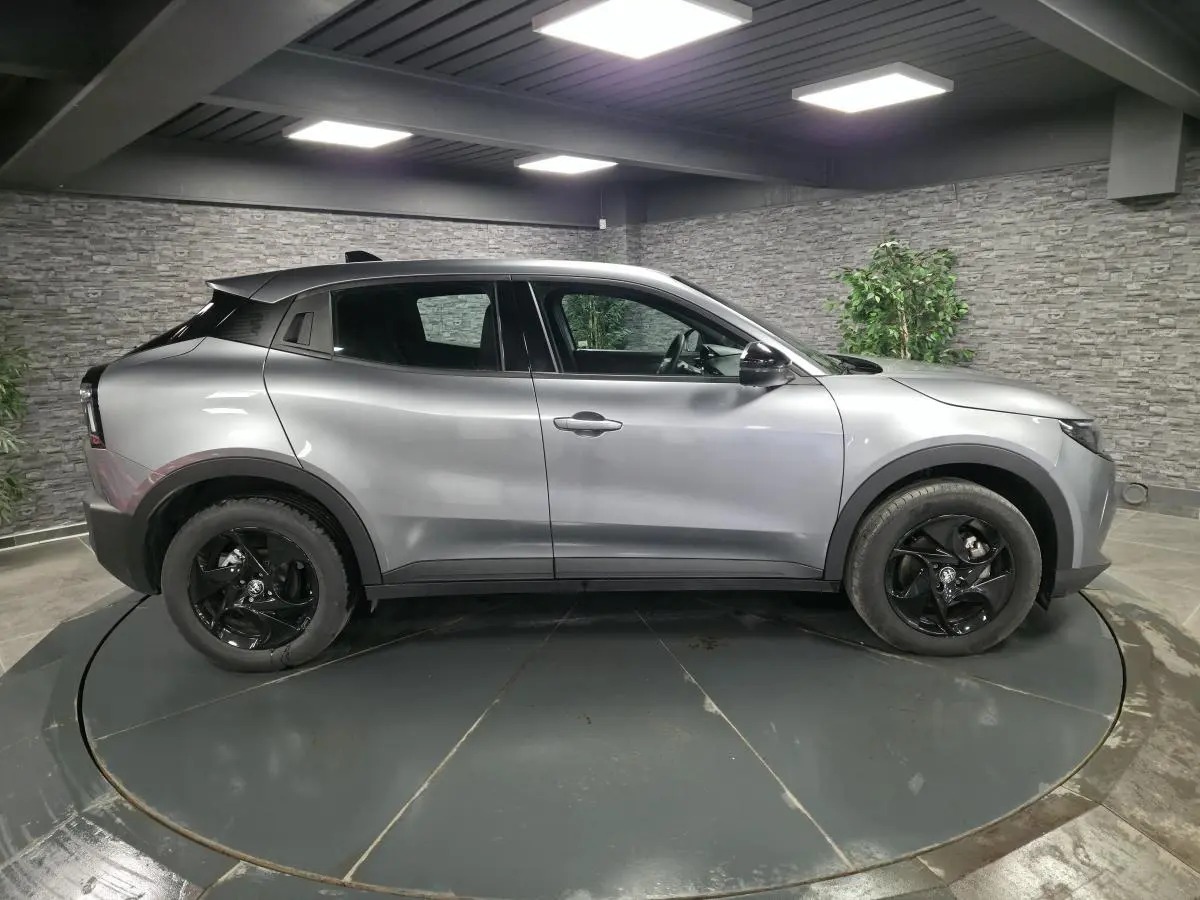 Vue de profil côté gauche d'une Alfa Romeo Junior 1.2 hybride gris métallisé avec jantes alliage noires dans un showroom.