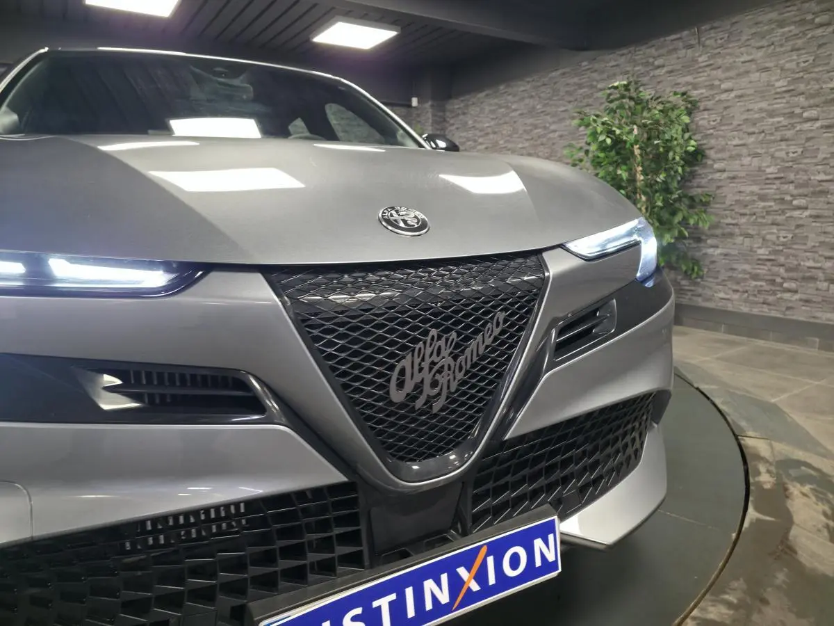 Vue avant rapprochée d'une Alfa Romeo Junior 1.2 Ibrida gris métallisé avec calandre noire et phares LED allumés.