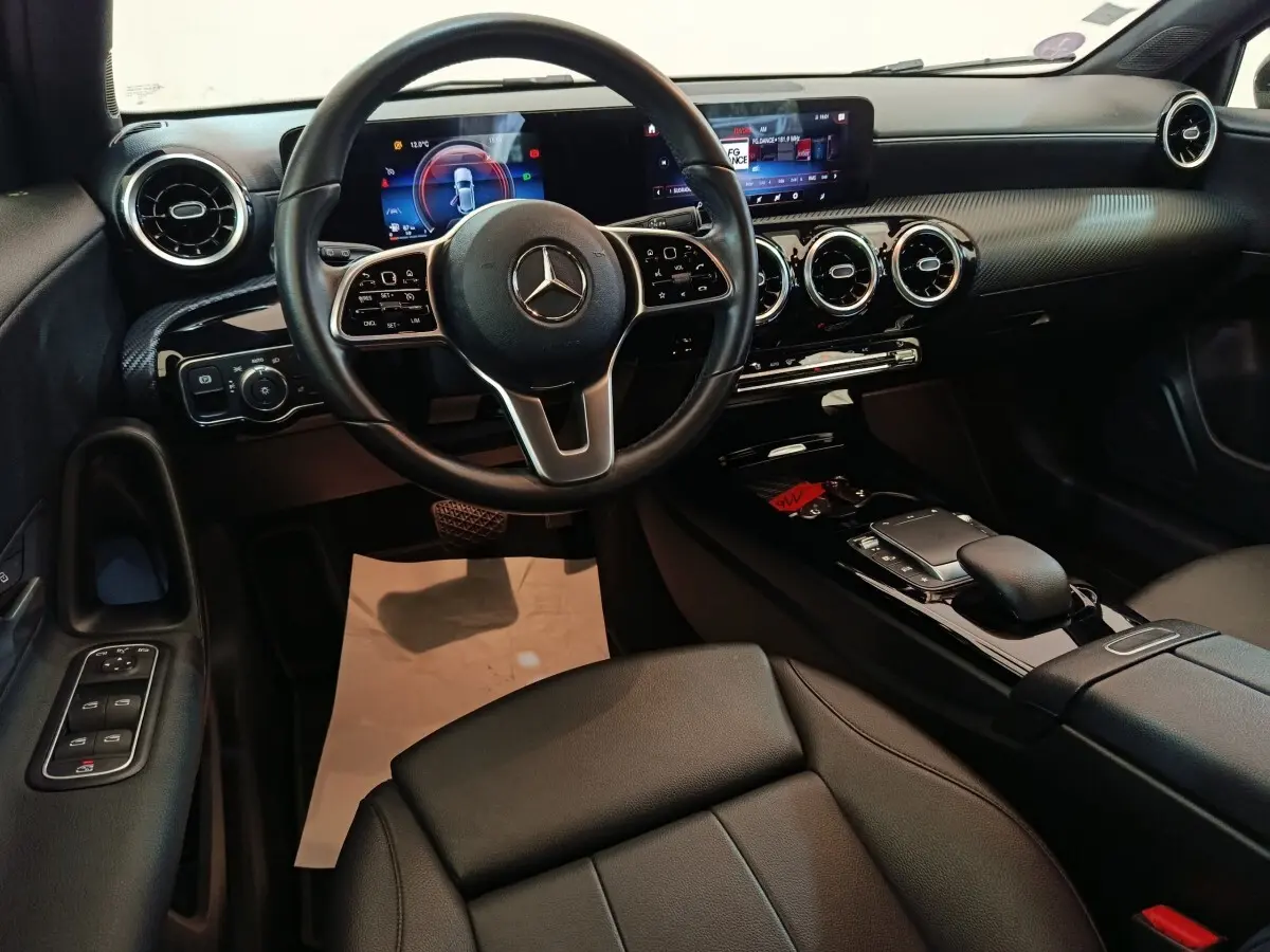 Vue intérieure de face du poste de conduite de la Mercedes Classe A 200 Business Line noire avec écran tactile et volant cuir multifonctions.