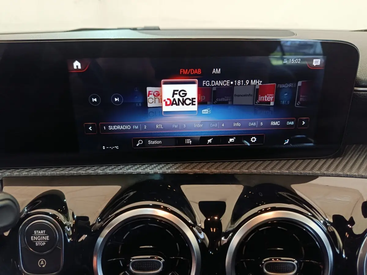 Gros plan sur l’écran tactile multimédia et les aérateurs ronds noirs du tableau de bord d’une Mercedes Classe A noire.