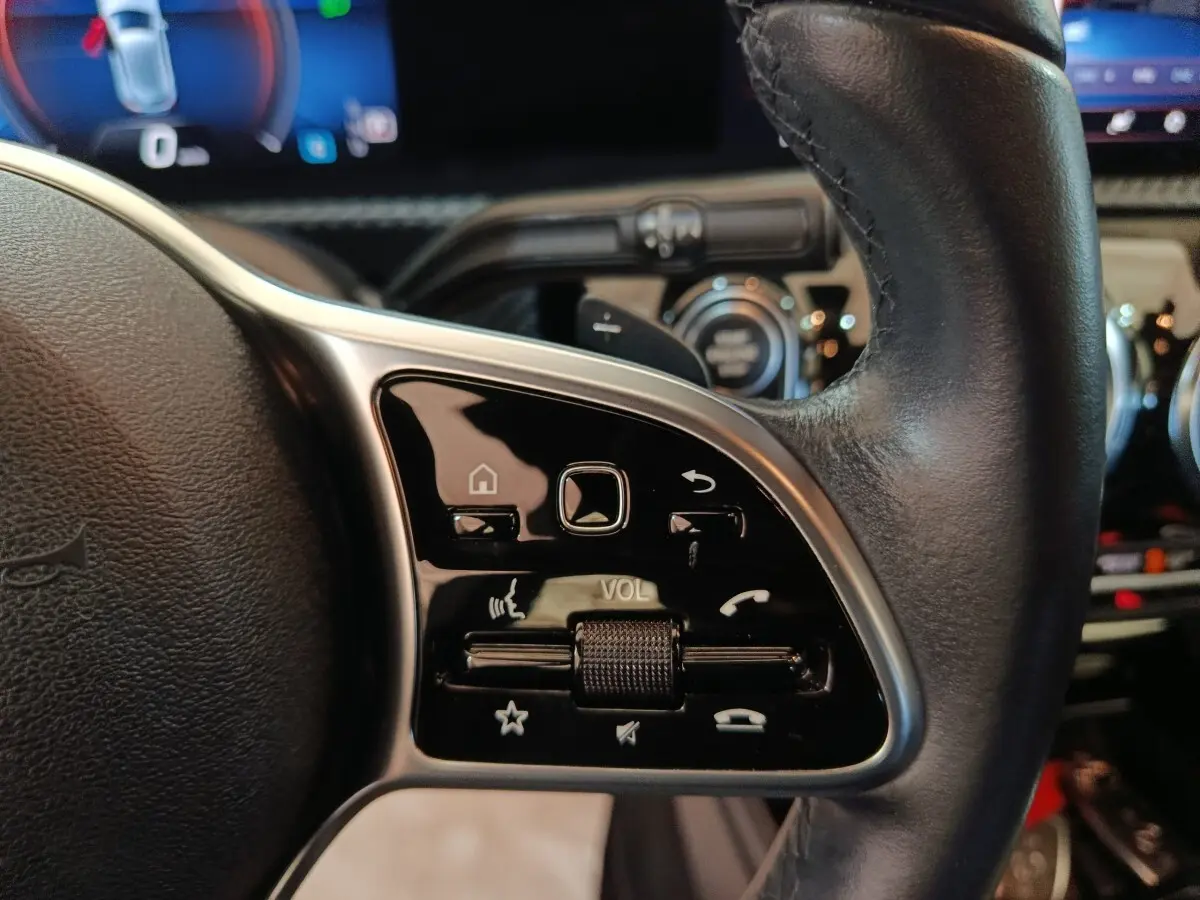 Gros plan sur les commandes multifonctions noires du volant cuir côté gauche de la Mercedes Classe A noire 2021.