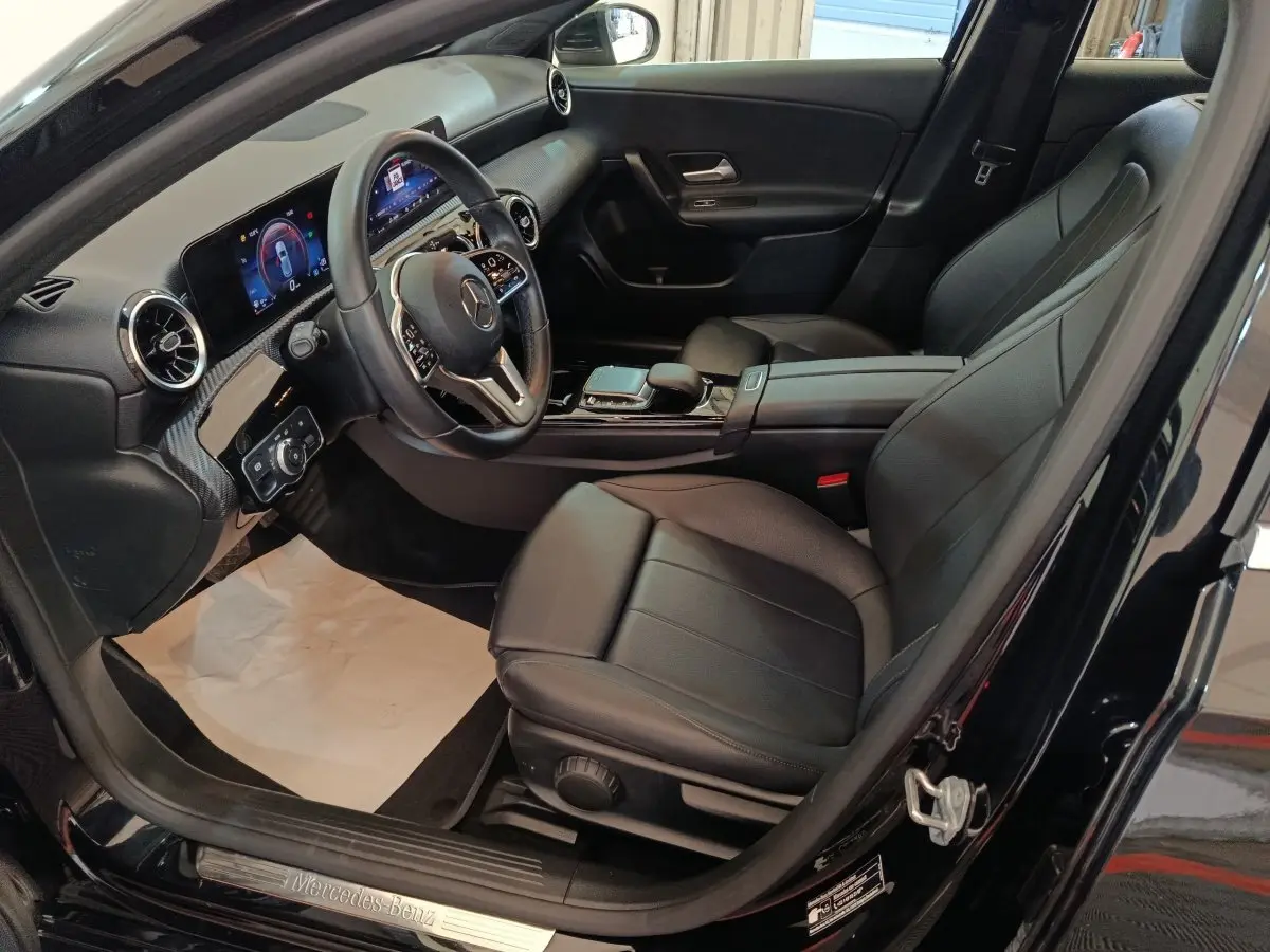 Vue intérieure côté conducteur de la Mercedes Classe A 200 Business Line noire, avec tableau de bord digital et sièges cuir noirs.