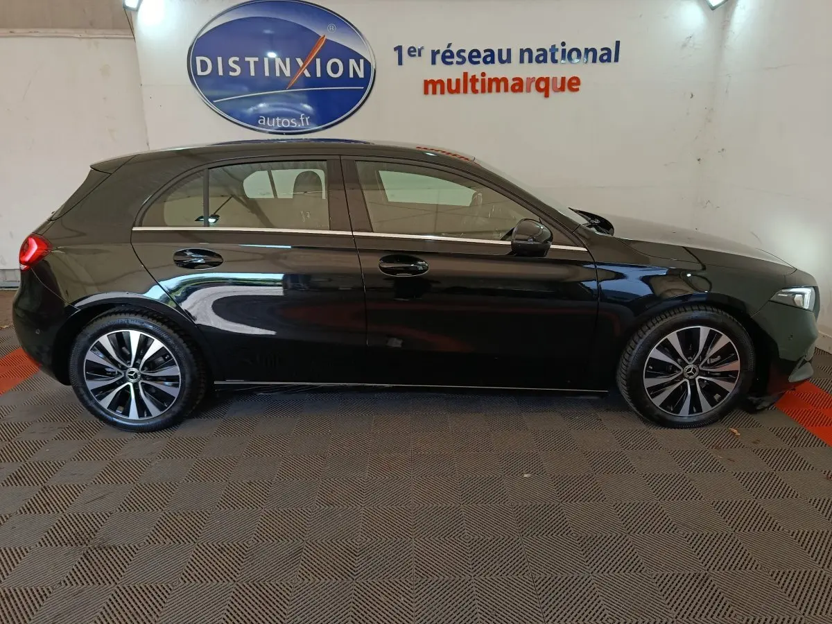 Profil latéral droit de la Mercedes Classe A 200 Business Line noire, avec jantes alliage et toit spoiler visible en intérieur showroom.