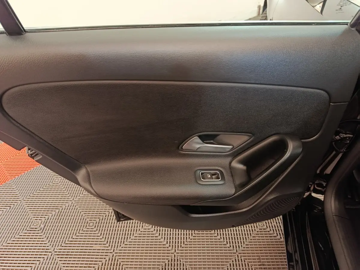 Vue intérieure côté gauche de la porte noire d'une Mercedes Classe A 200 Business Line 2021 avec poignée et commande de fenêtre.
