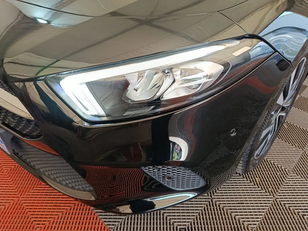 Gros plan sur le phare avant droit noir brillant de la Mercedes Classe A 200 Business Line 2021 avec jante visible.