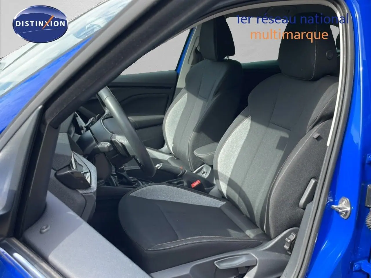 Vue intérieure côté conducteur d'une Skoda Scala bleu racing metal, sièges tissu gris et noir avec surpiqûres.