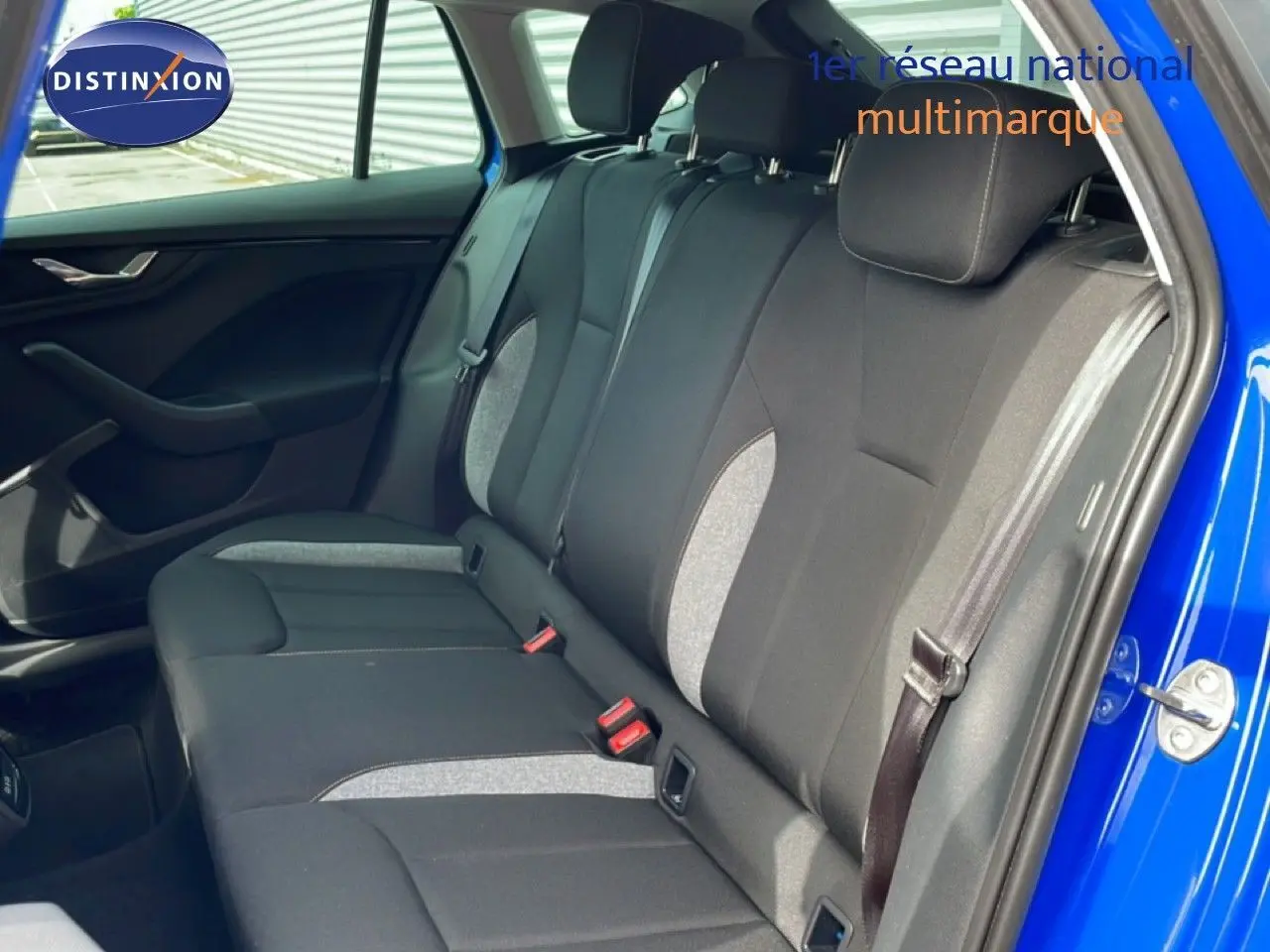 Vue intérieure côté arrière droit de la Skoda Scala 2025 en bleu Racing Metal, sièges tissu gris et noir avec ceintures visibles.