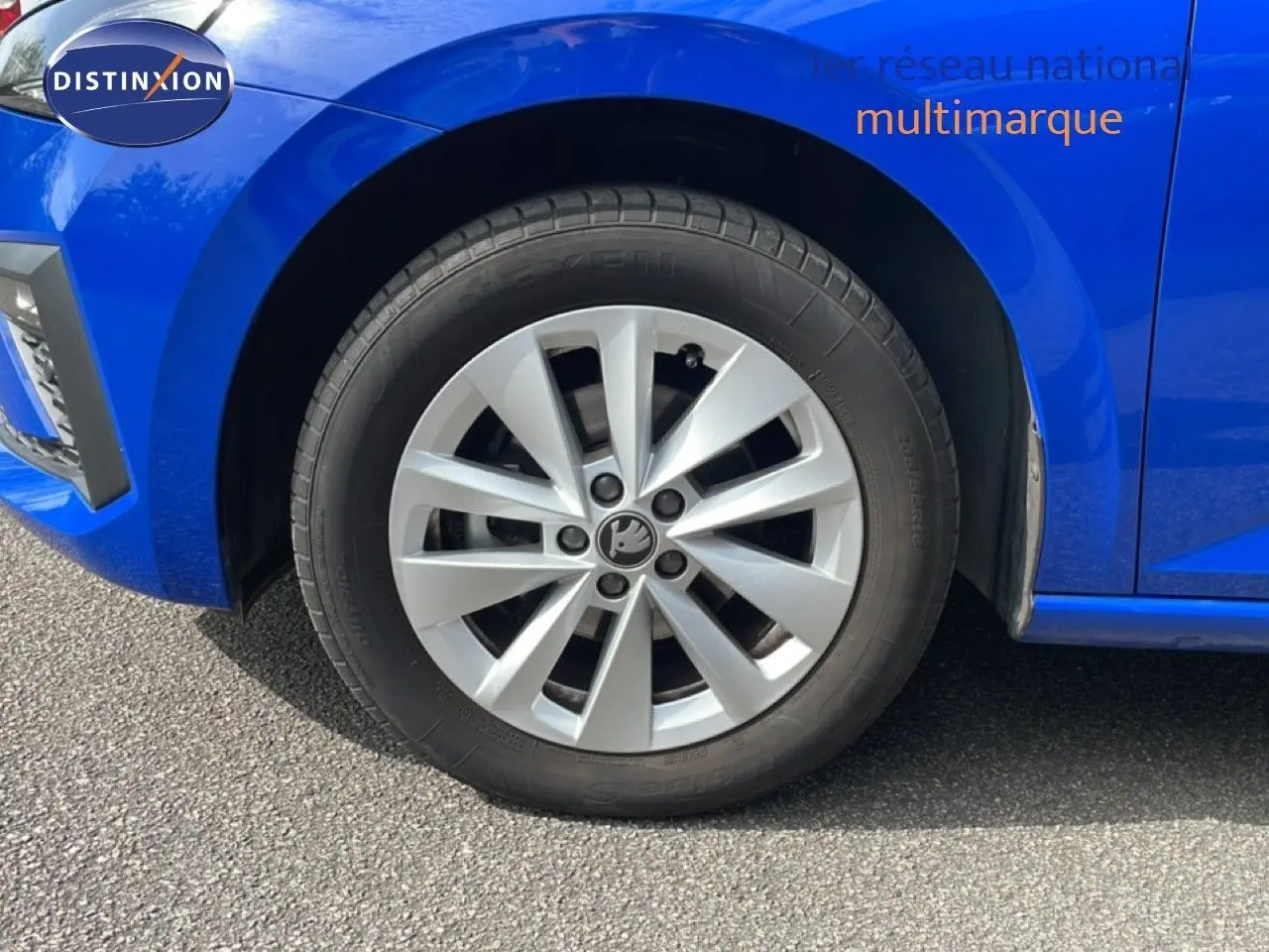 Gros plan sur la roue avant gauche d'une Skoda Scala bleu racing metal, avec jante argentée à plusieurs branches.