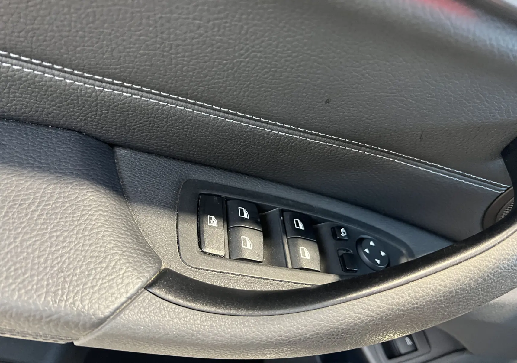 Gros plan sur les commandes des vitres côté conducteur d'un BMW X1 F48 noir avec surpiqûres blanches sur la porte.