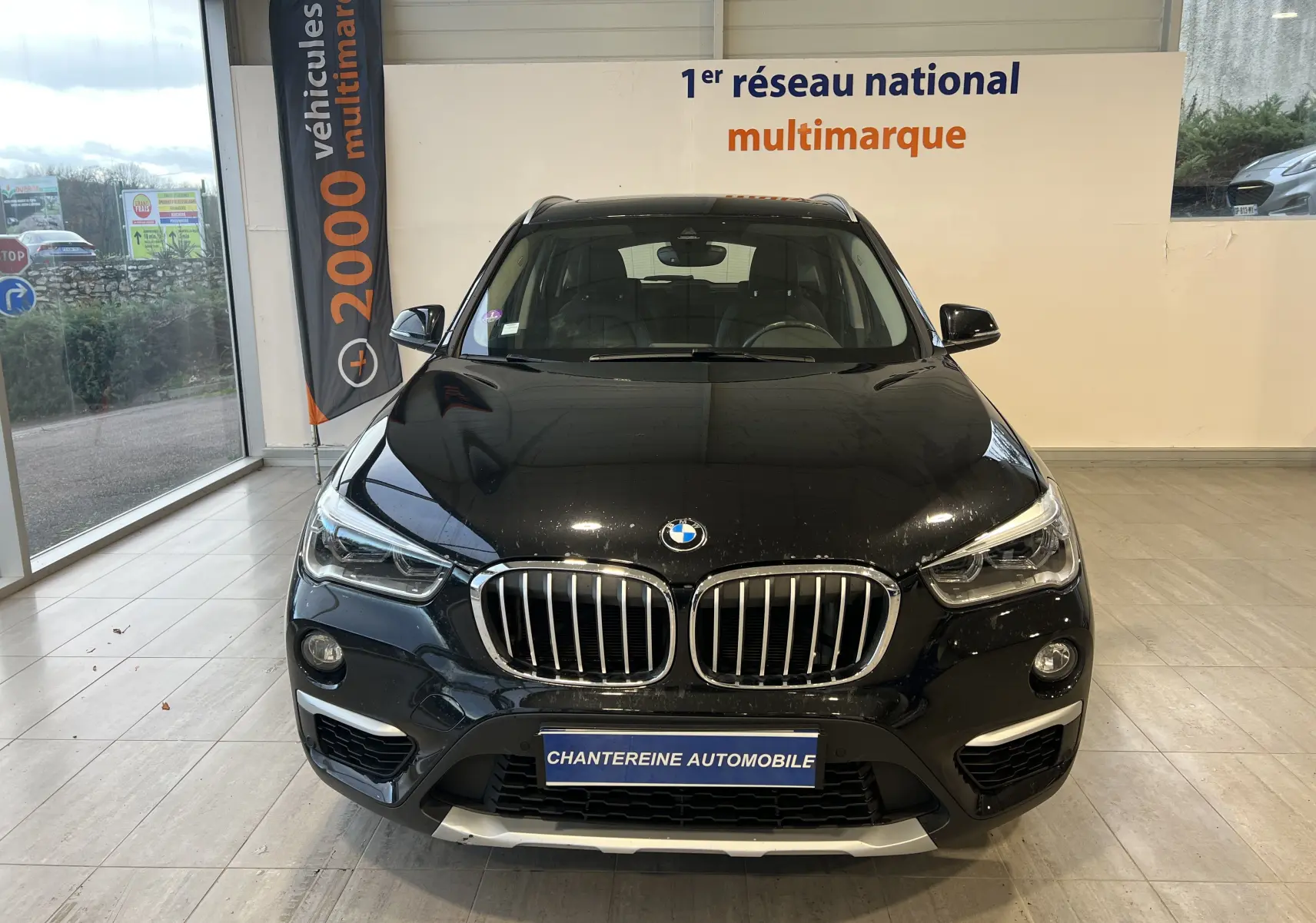 Vue frontale d'un BMW X1 F48 noir Saphirschwarz avec calandre double haricot et phares LED en showroom.