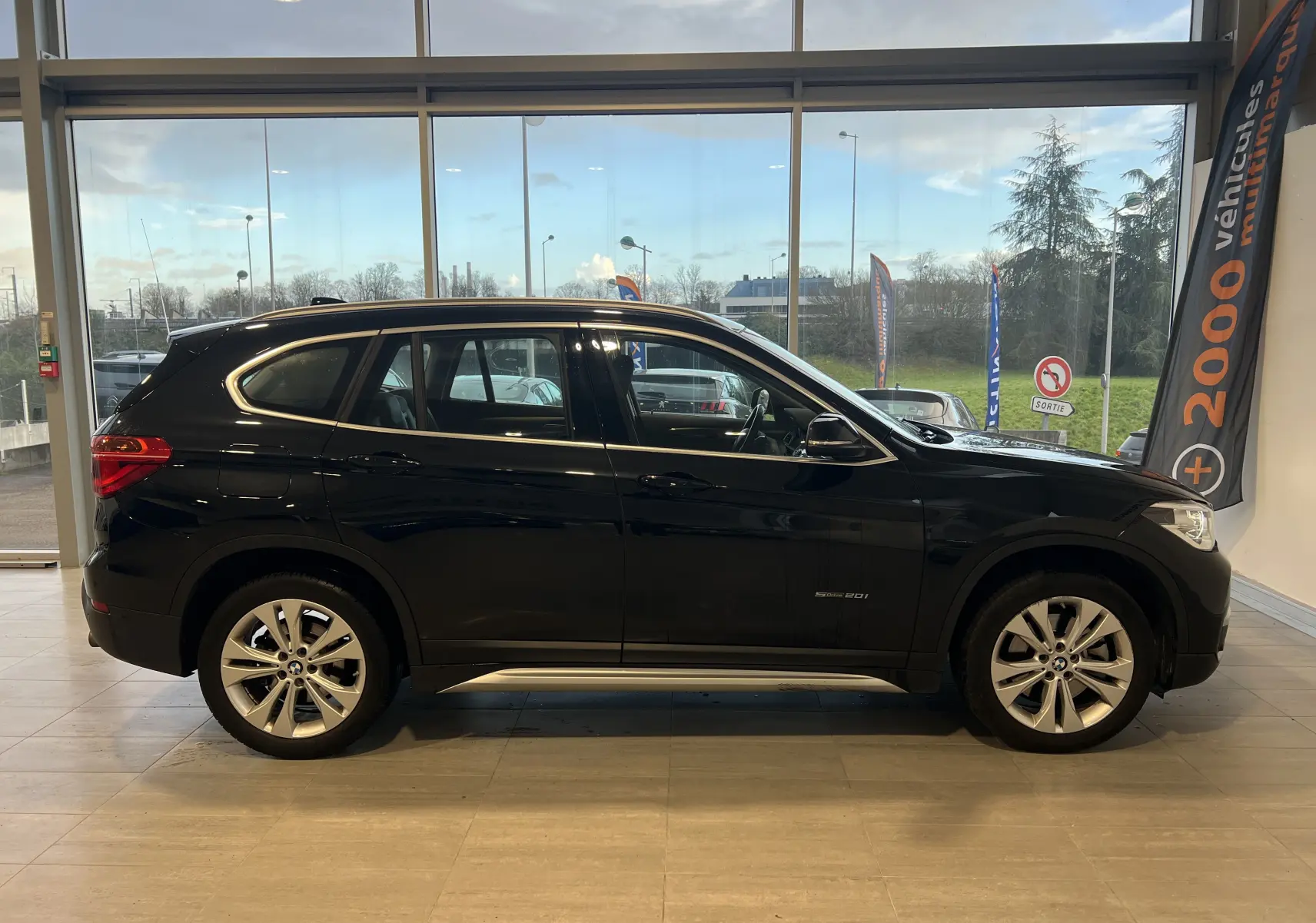 Profil côté gauche du BMW X1 F48 noir Saphirschwarz en version sDrive16d Lounge, visible en intérieur showroom.
