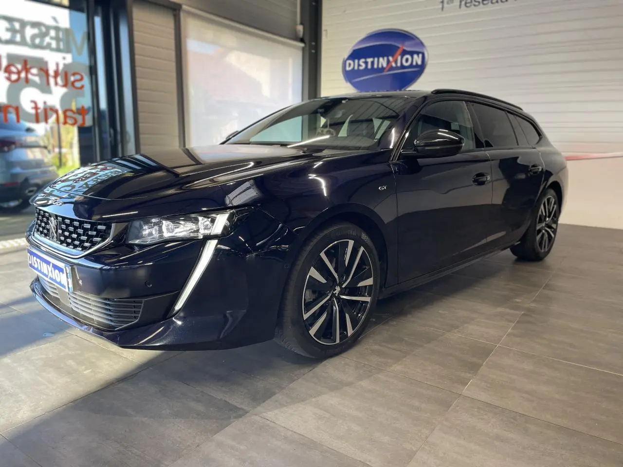 Peugeot 508 SW bleu foncé vue 3/4 avant droit en intérieur avec jantes alliage et calandre distinctive.