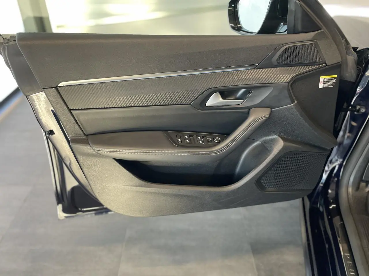 Vue latérale du panneau de porte avant gauche en cuir noir et inserts carbone du Peugeot 508 SW bleu foncé.