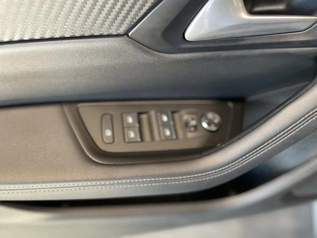 Gros plan sur les commandes de lève-vitres et rétroviseurs côté conducteur d'une Peugeot 508 SW bleu foncé.
