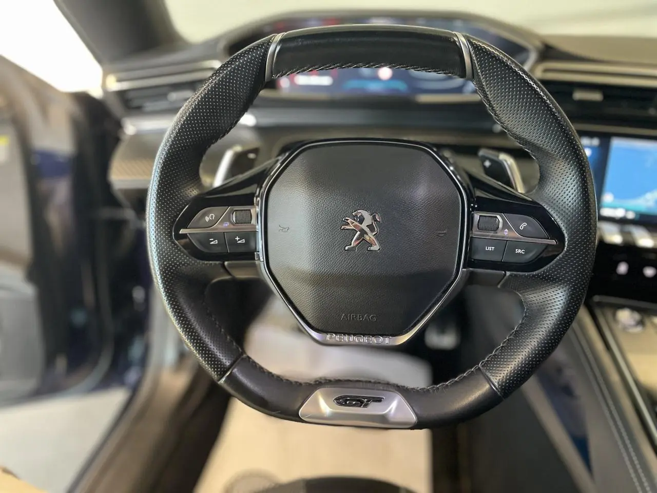 Volant noir perforé avec logo Peugeot et badge GT, vue frontale de l'intérieur du break 508 SW bleu foncé.