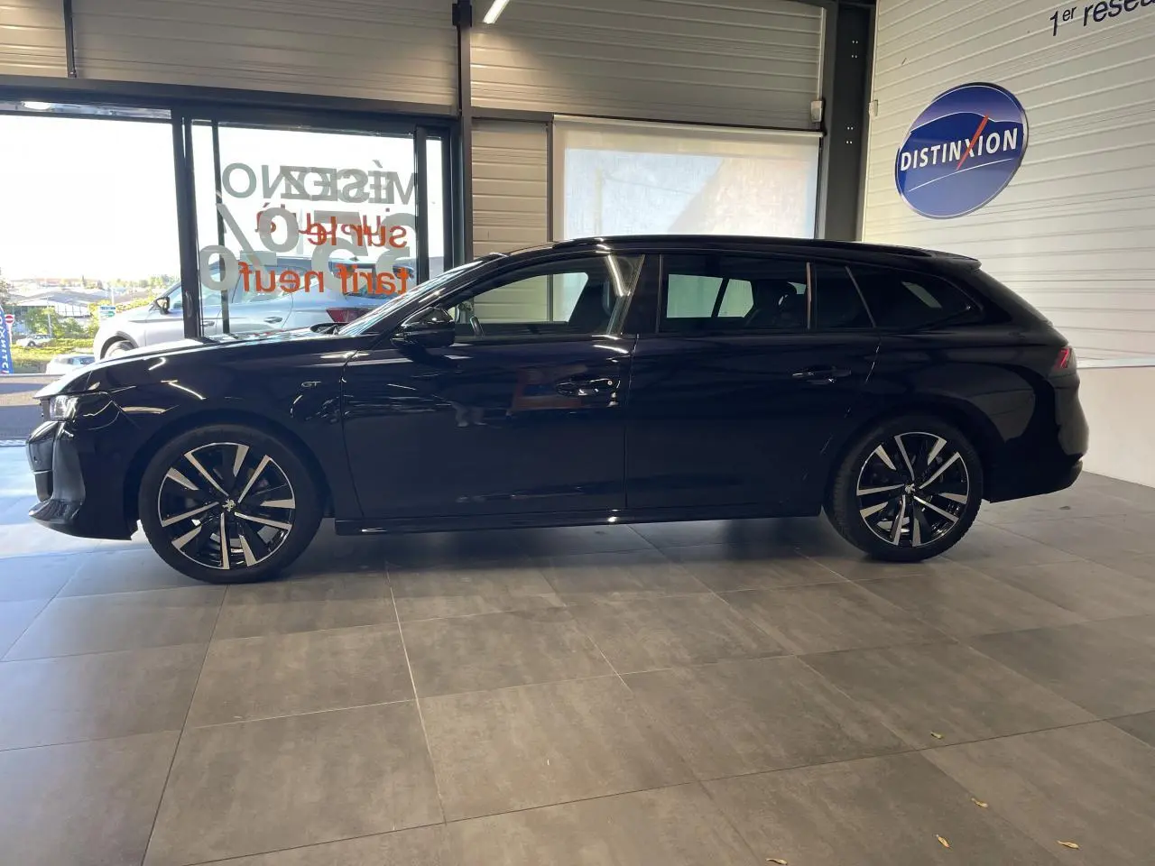 Peugeot 508 SW bleu foncé vue de profil côté gauche en intérieur, avec jantes alliage bi-ton et badge GT visible.