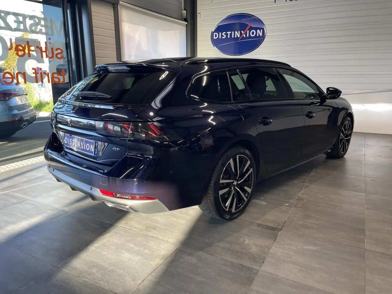 Peugeot 508 SW bleu foncé vue 3/4 arrière droit en intérieur avec jantes alliage et logo GT visible.