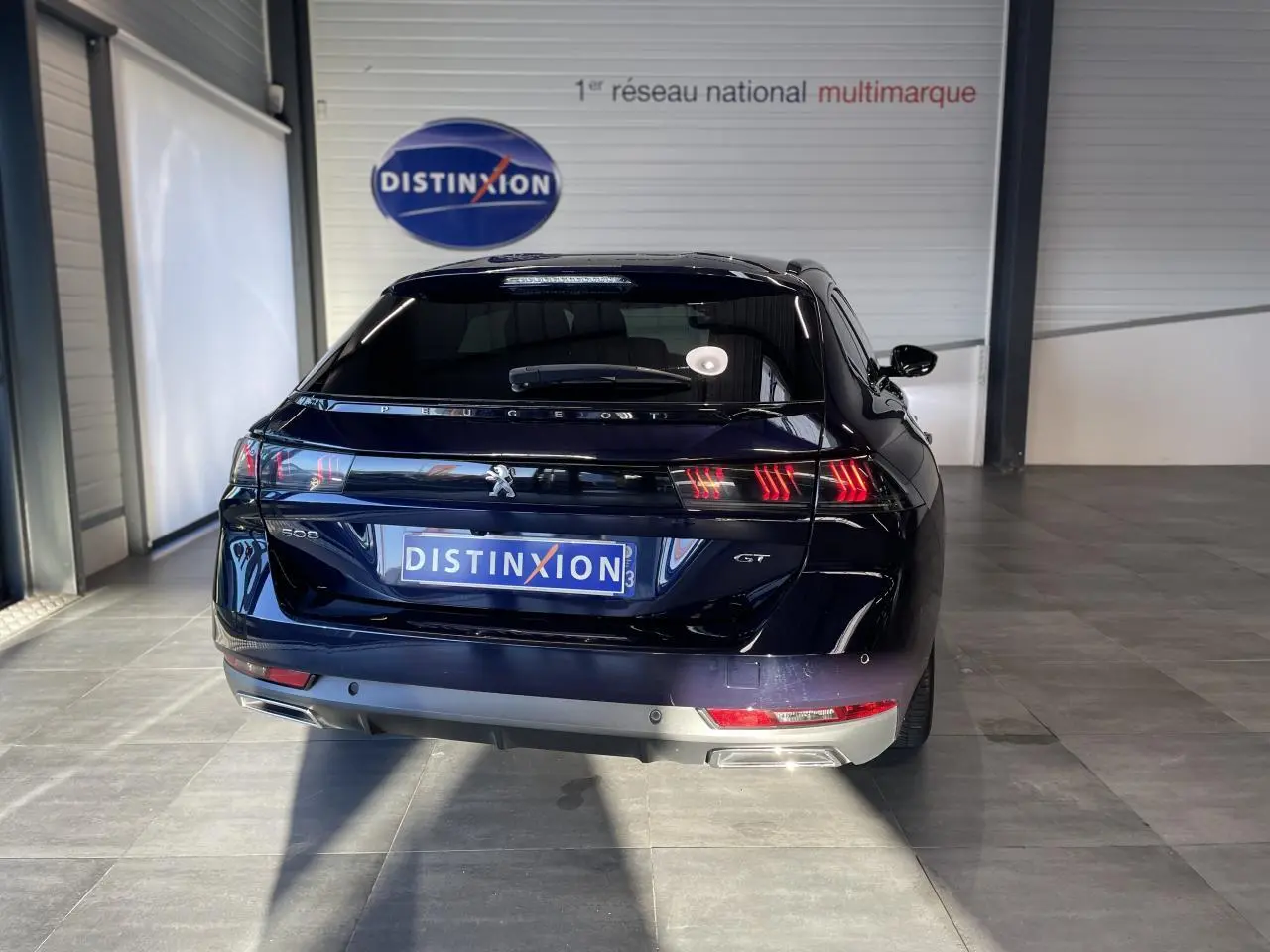 Vue arrière d'une Peugeot 508 SW bleu foncé avec feux arrière allumés et logo GT visible en intérieur showroom.