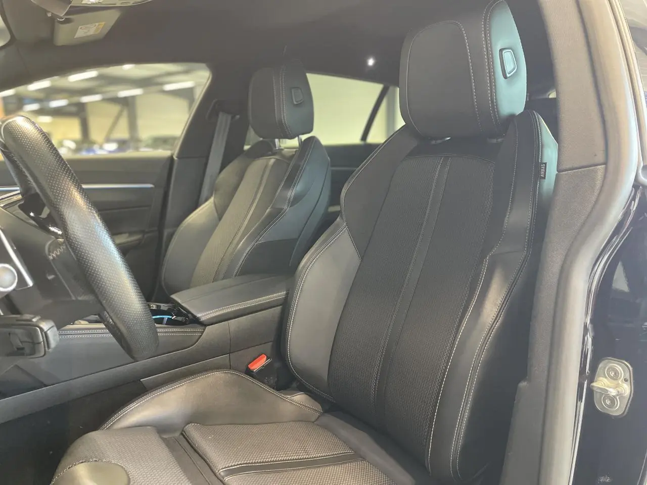 Gros plan sur les sièges avant en cuir noir de la Peugeot 508 SW, avec coutures apparentes et appuie-têtes intégrés.