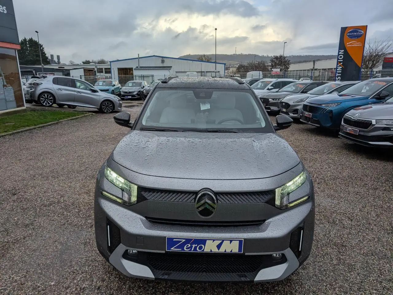 Vue avant d'un Citroën C3 Aircross gris métallisé avec toit noir et phares LED allumés sous la pluie.