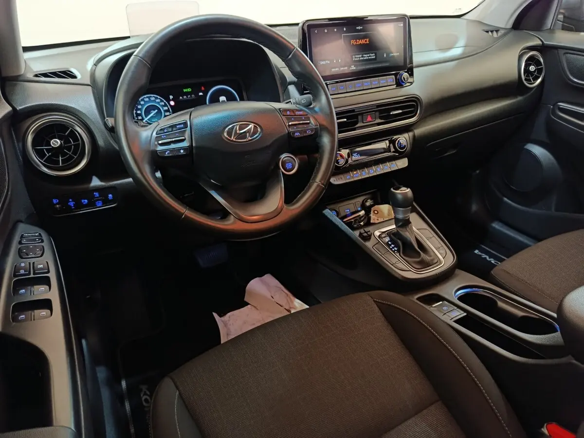 Vue intérieure avant droite du Hyundai Kona 1.6 Hybrid 2023, volant cuir multifonctions et écran tactile central allumé.