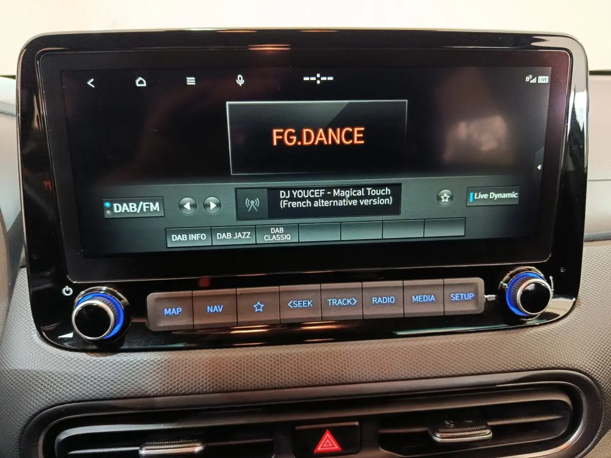 Écran tactile central du tableau de bord du Hyundai Kona gris foncé, affichant une radio DAB/FM avec commandes en dessous.