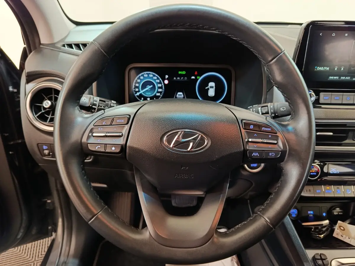 Vue intérieure centrée sur le volant cuir multifonctions du Hyundai Kona 1.6 Hybrid 2023 avec tableau de bord digital.