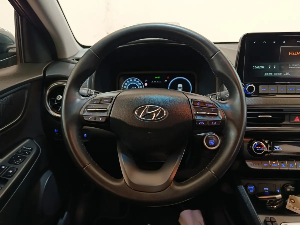 Vue intérieure centrée sur le volant cuir multifonctions d'une Hyundai Kona 1.6 Hybrid 2023 avec tableau de bord numérique.