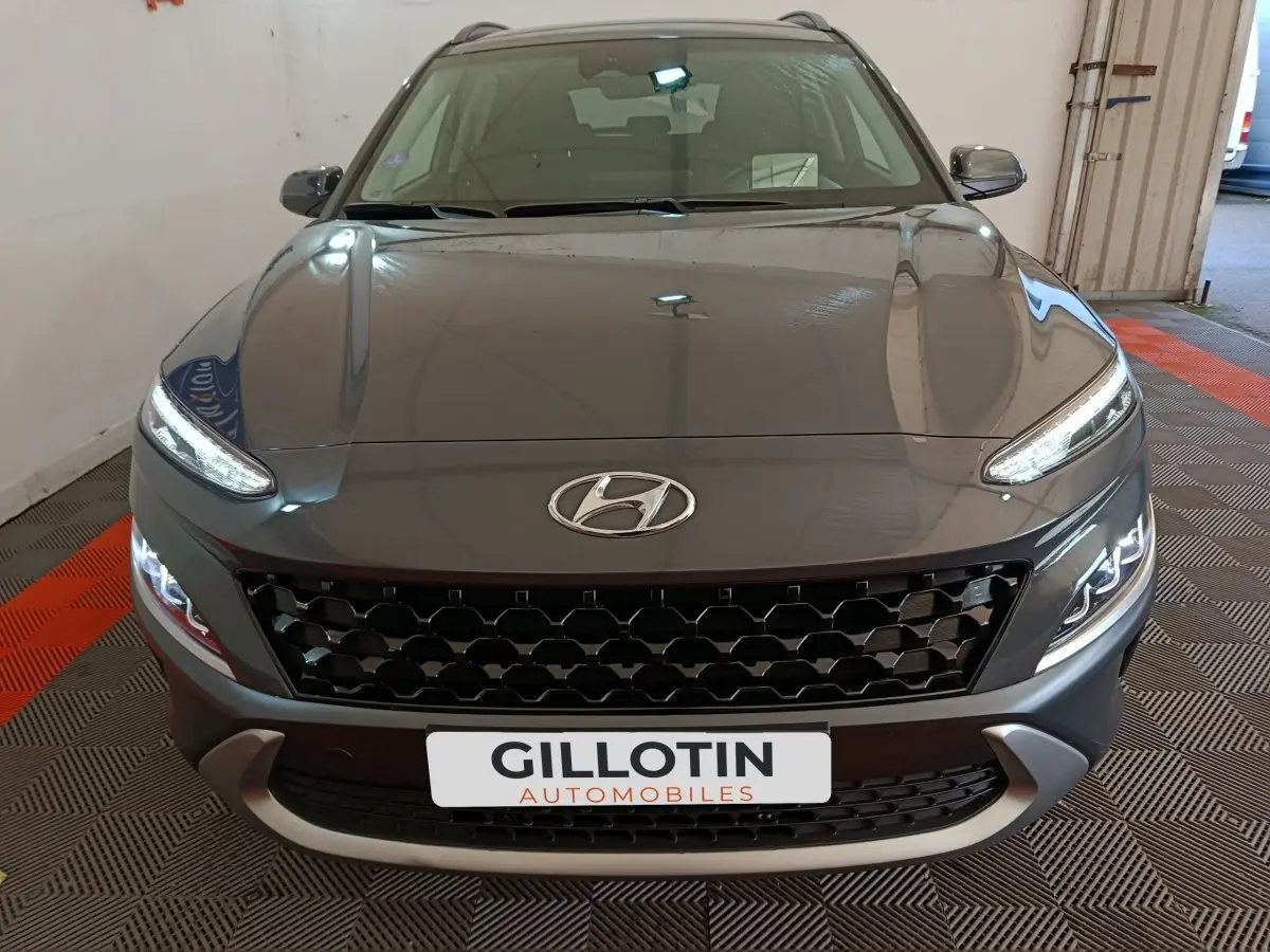 Vue avant d’un Hyundai Kona gris foncé 2023 avec calandre noire et feux LED allumés dans un garage.