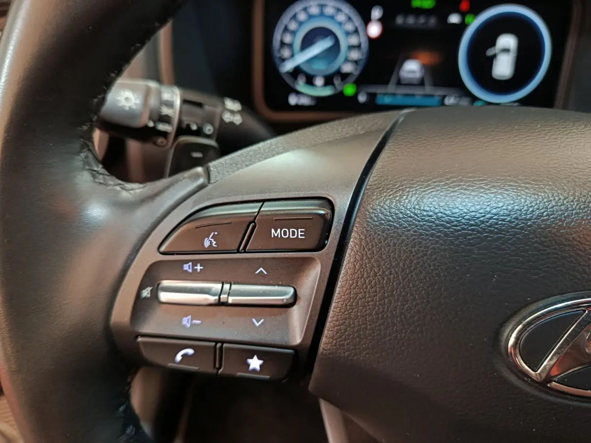 Gros plan sur le volant cuir noir du Hyundai Kona 2023, avec commandes multifonctions et tableau de bord numérique en arrière-plan.