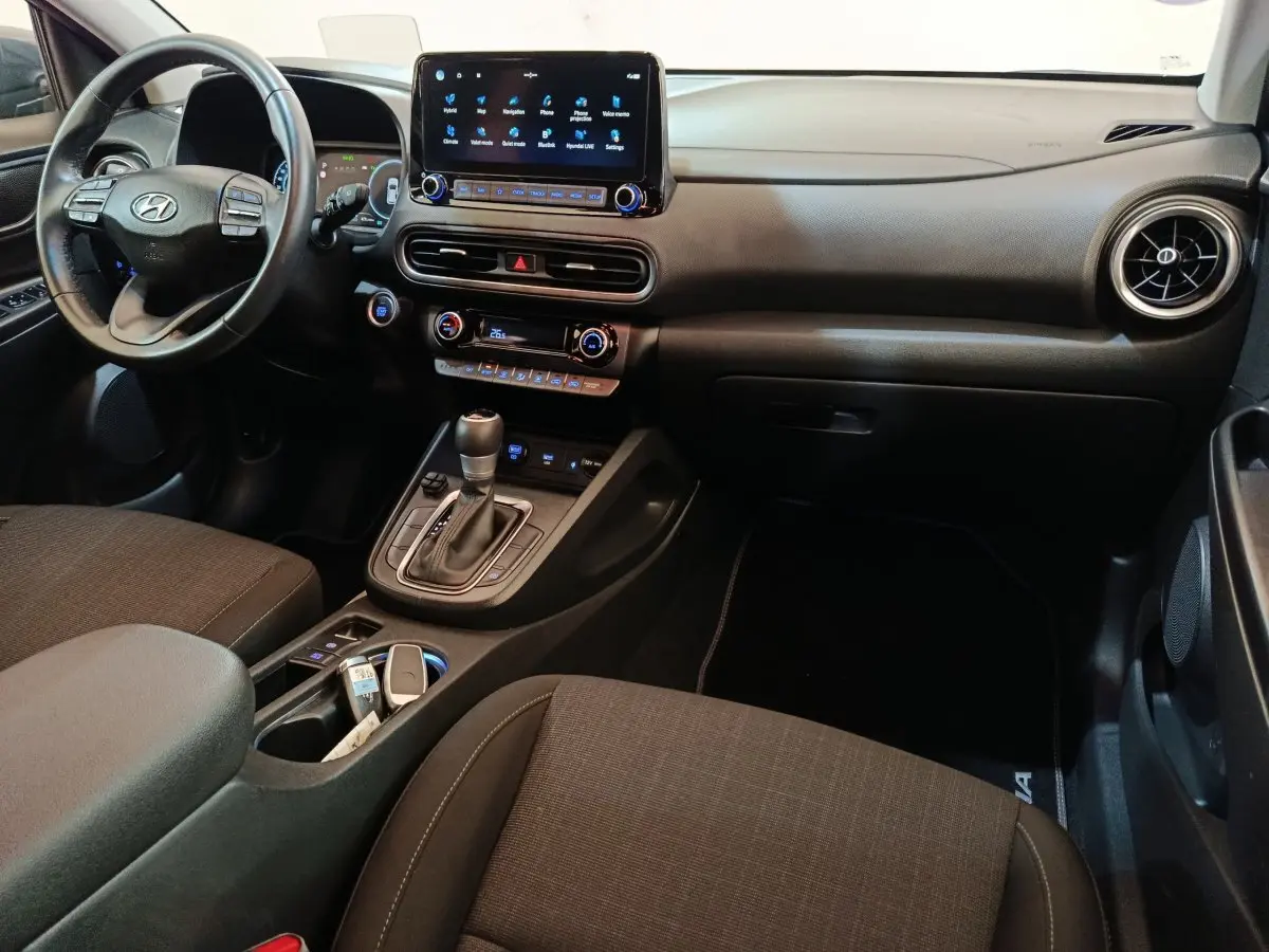 Vue intérieure côté conducteur du Hyundai Kona 1.6 Hybrid 2023, avec tableau de bord noir et écran tactile central.