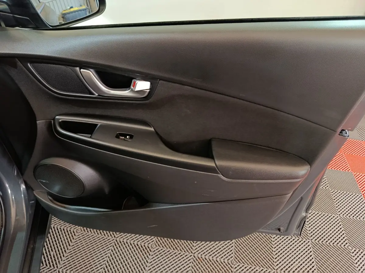 Vue intérieure côté gauche de la porte avant gris foncé du Hyundai Kona 1.6 Hybrid 2023 avec poignée et haut-parleur intégrés.