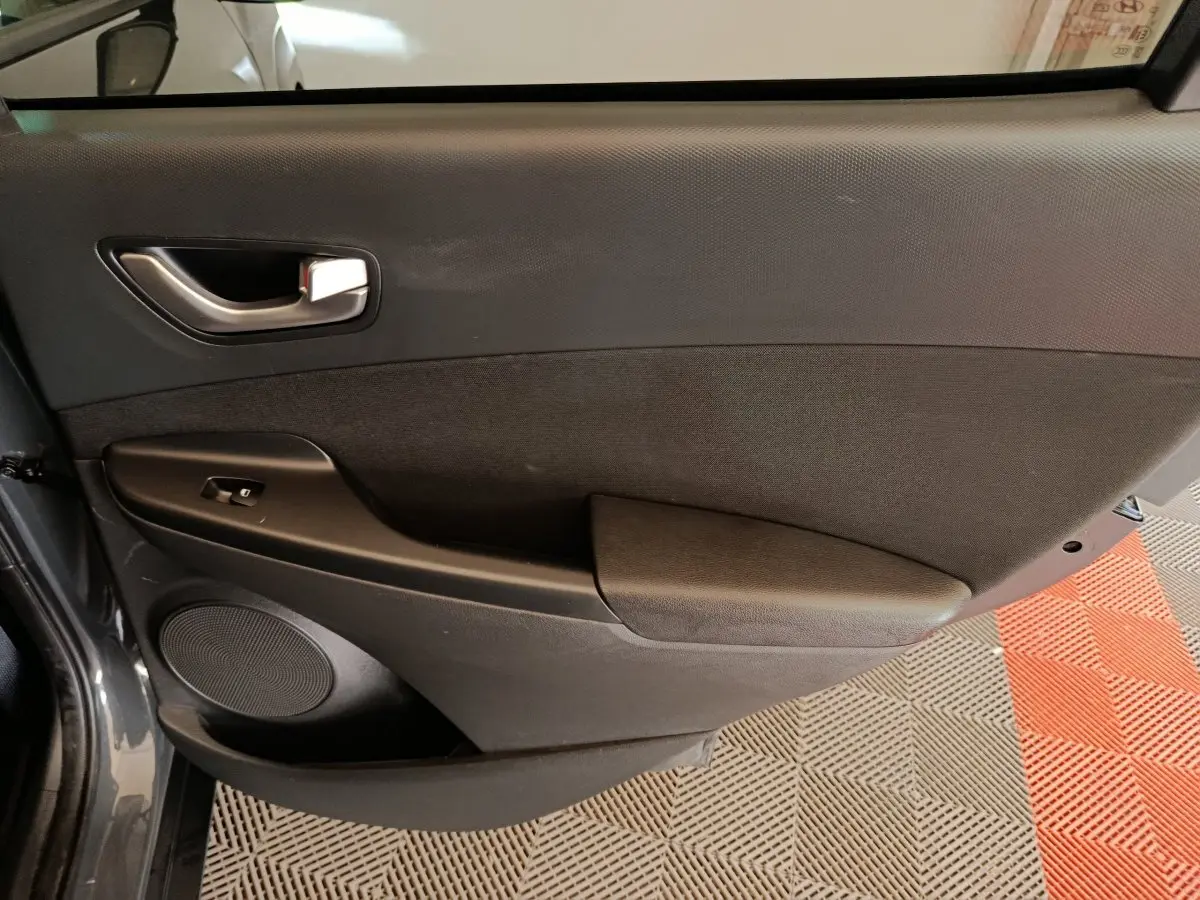 Vue intérieure du panneau de porte avant gauche gris foncé du Hyundai Kona 2023 avec commande de fenêtre électrique.