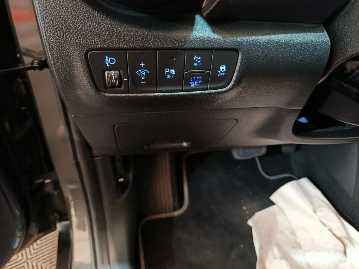 Vue intérieure du tableau de bord côté gauche du Hyundai Kona gris foncé, avec commandes éclairage et assistance au stationnement.